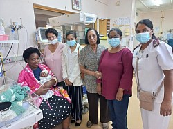 Group of women and a nurse in a hospital talking to a new mum with her newborn baby